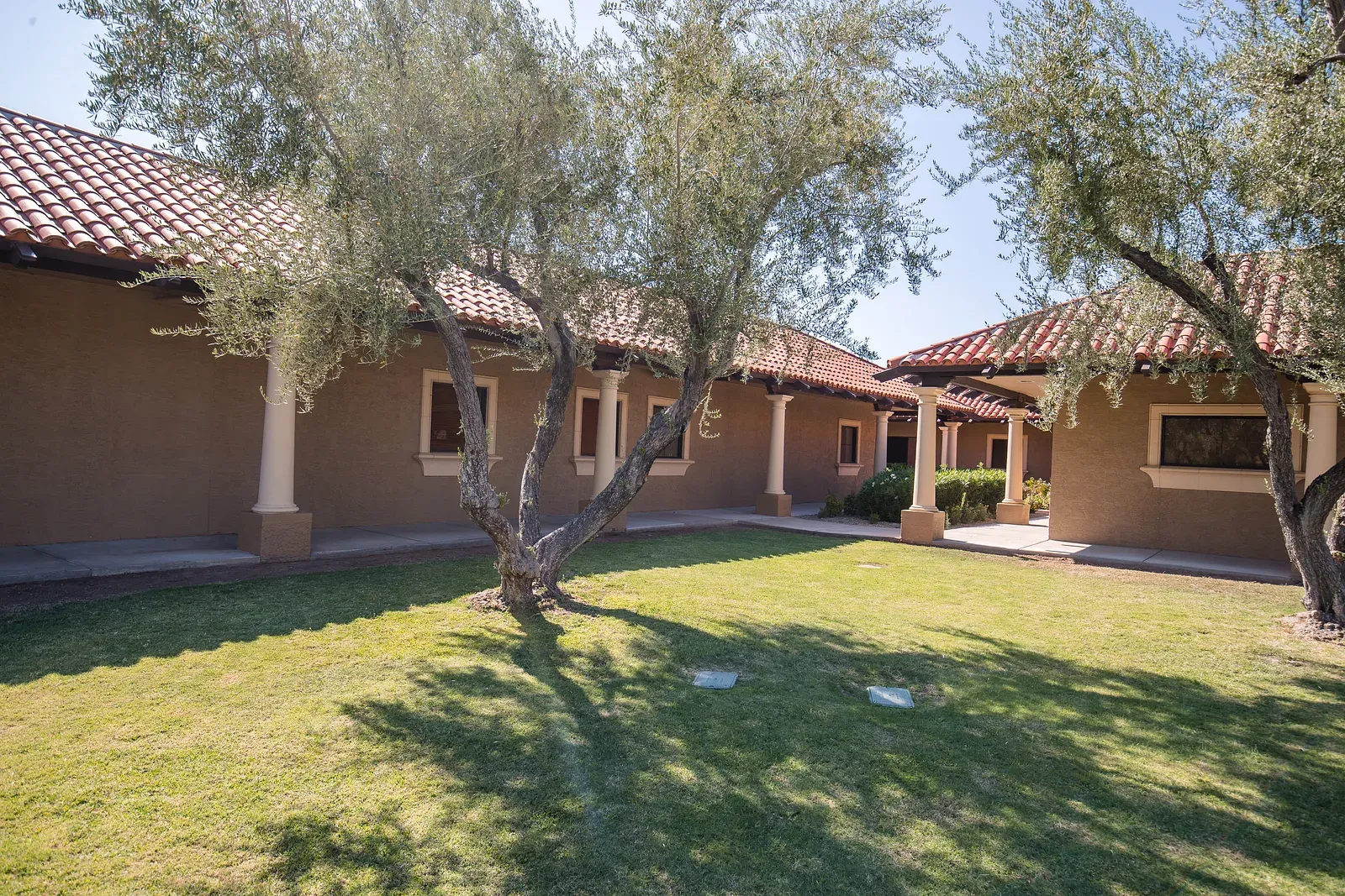 The mission-style courtyard at Sonoran Sleep Center in Glendale, Arizona — olive trees, green lawn and red-tile roofs under a clear desert sky